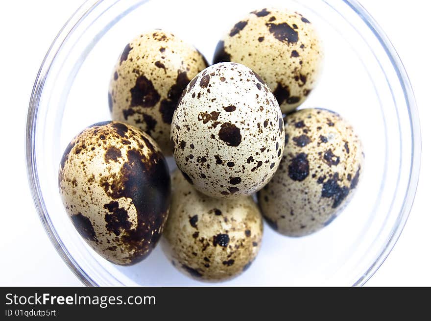 Overhead shot of quail eggs in glass bowl on white background