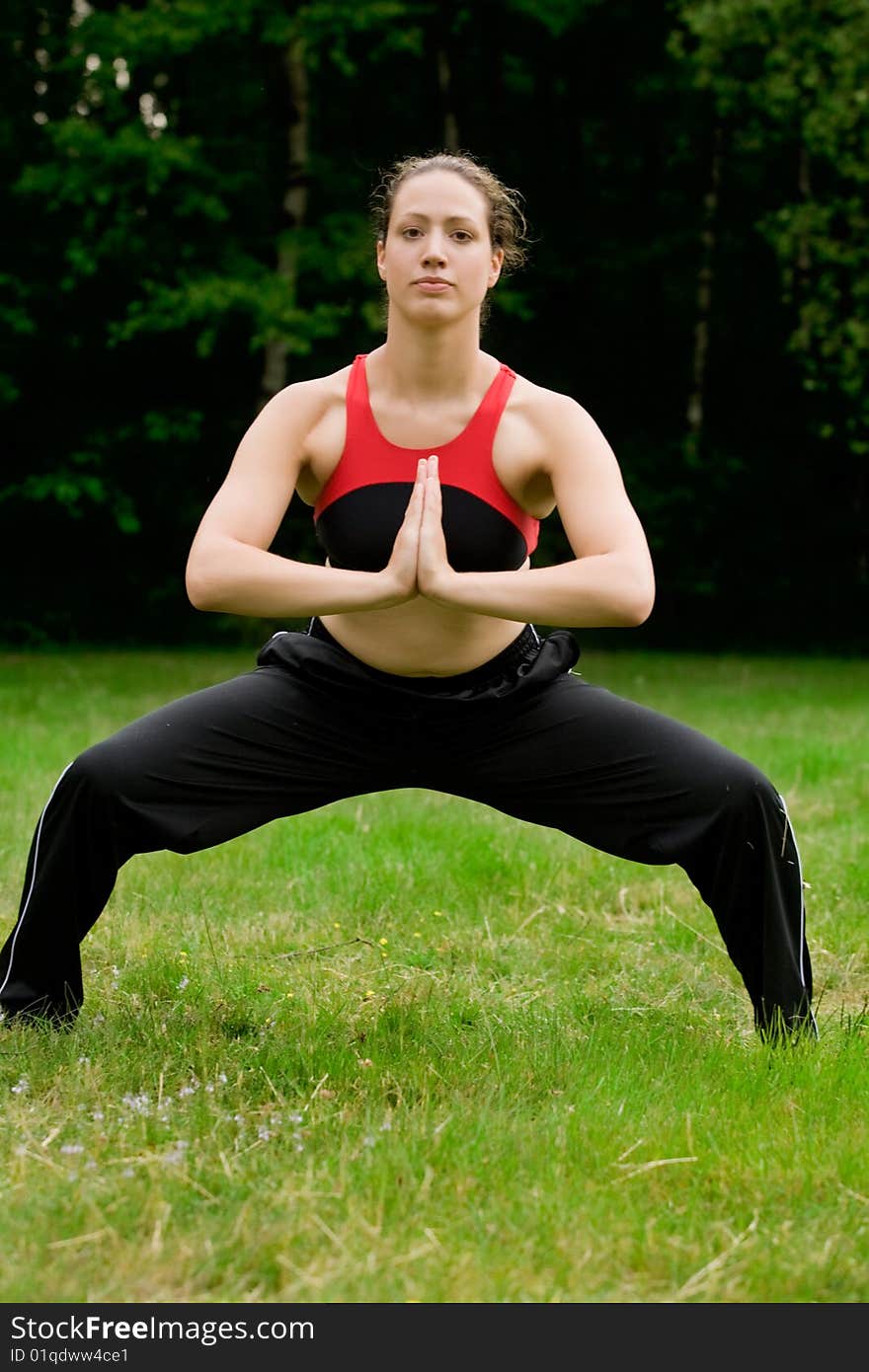 Practising Yoga In A Green Field With Trees