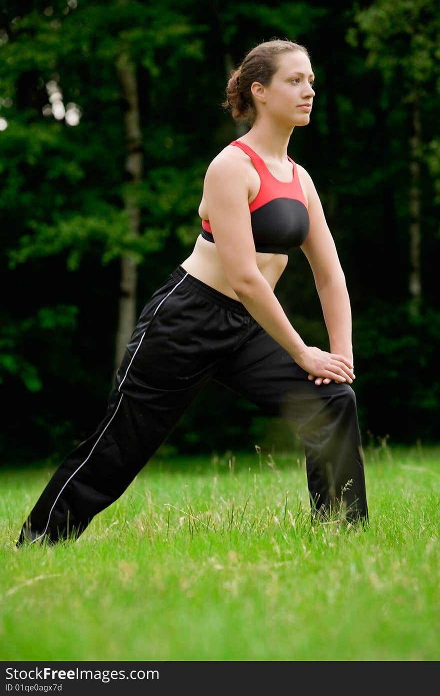 Practising Yoga In A Green Field With Trees