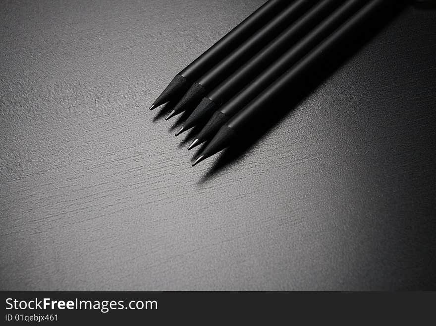 Five black pencils over black leather background