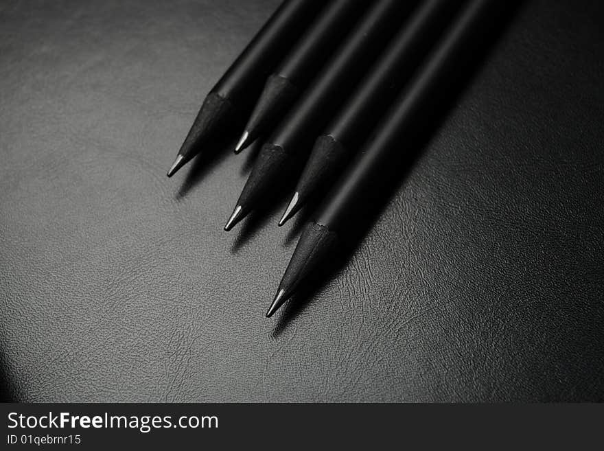 Five black pencils over black leather background