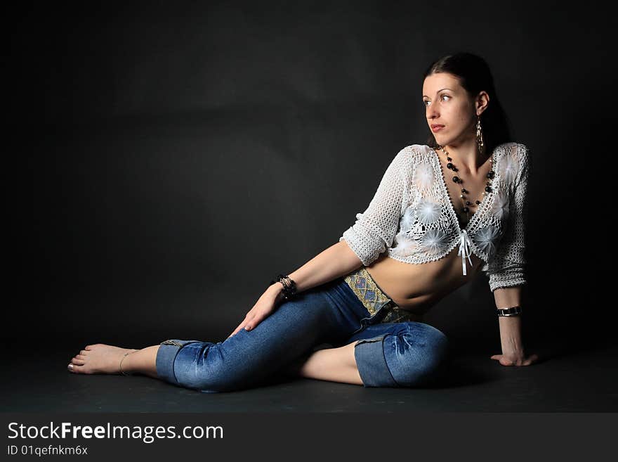 Young slim girl sitting on the floor over black background