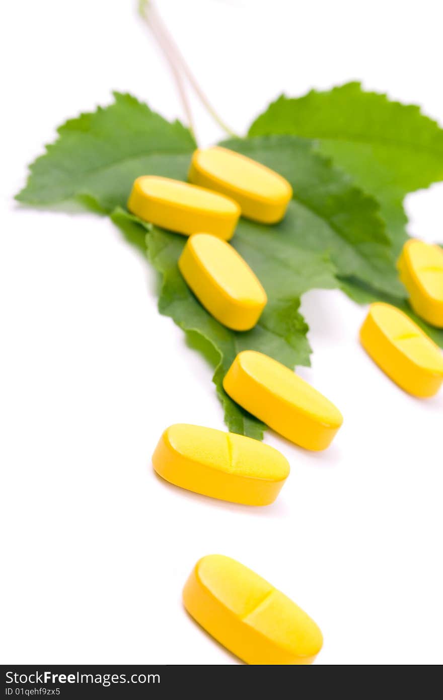 Yellow vitamin pills over green leaves on white background