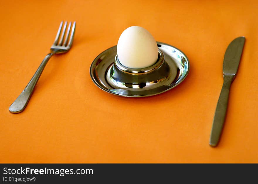 Egg, holder, fork and knife over brown tablecloth. Egg, holder, fork and knife over brown tablecloth