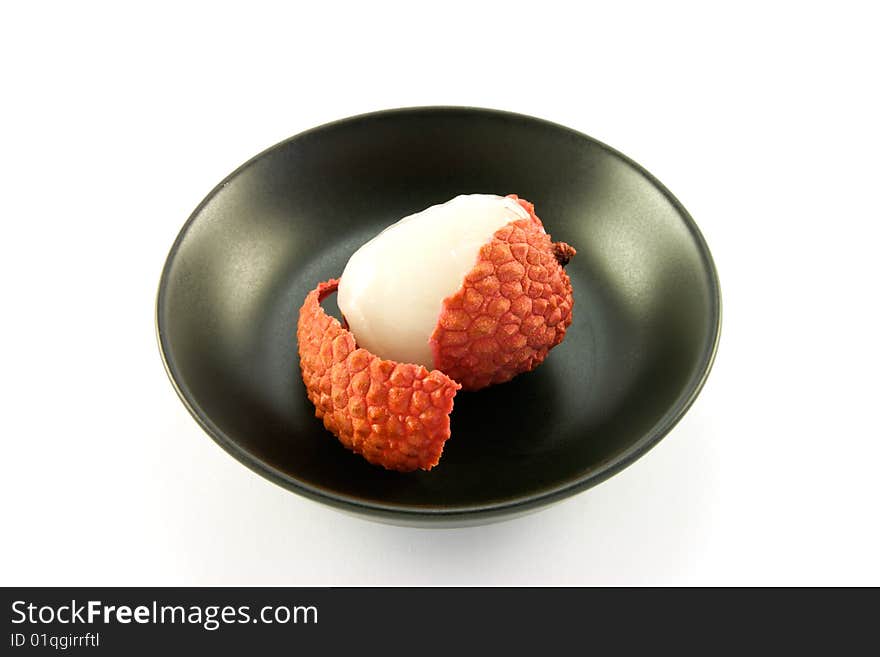 Single peeled lychee in a black dish with clipping on a white background