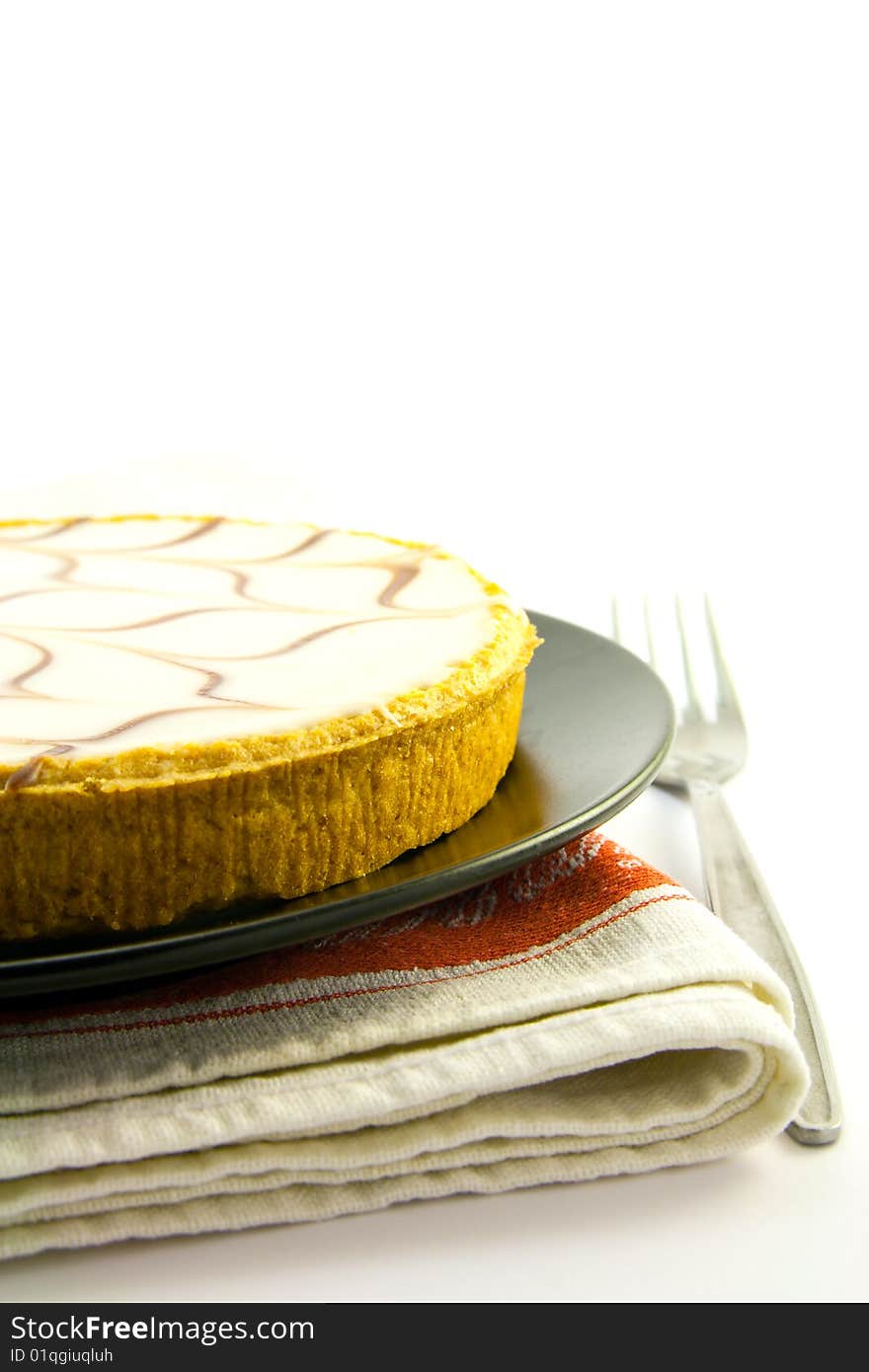 Delicious looking iced bakewell tart on a black plate with a plain background