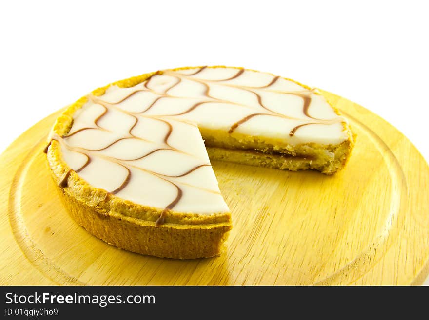 Delicious looking iced bakewell tart on a wooden platter with a plain background