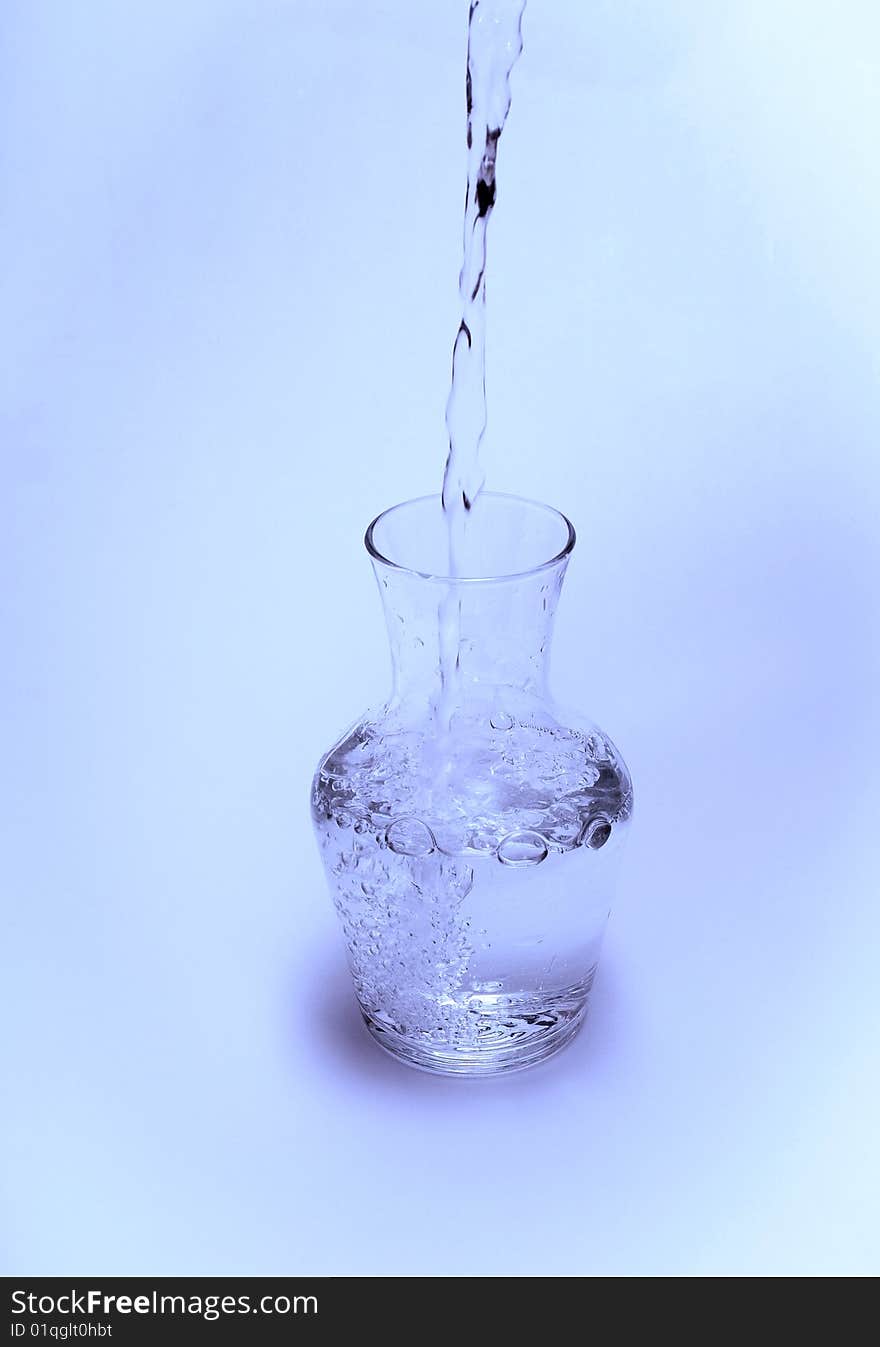 View of water being poured into a glass carafe on a blue background. View of water being poured into a glass carafe on a blue background