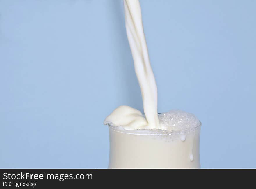 View of milk being poured into a glass carafe on a blue background. View of milk being poured into a glass carafe on a blue background