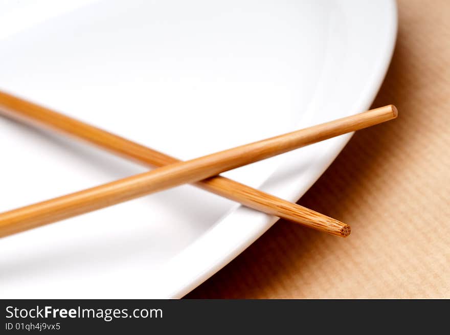 A tilted horizontal macro of a pair of chopsticks on a white plate