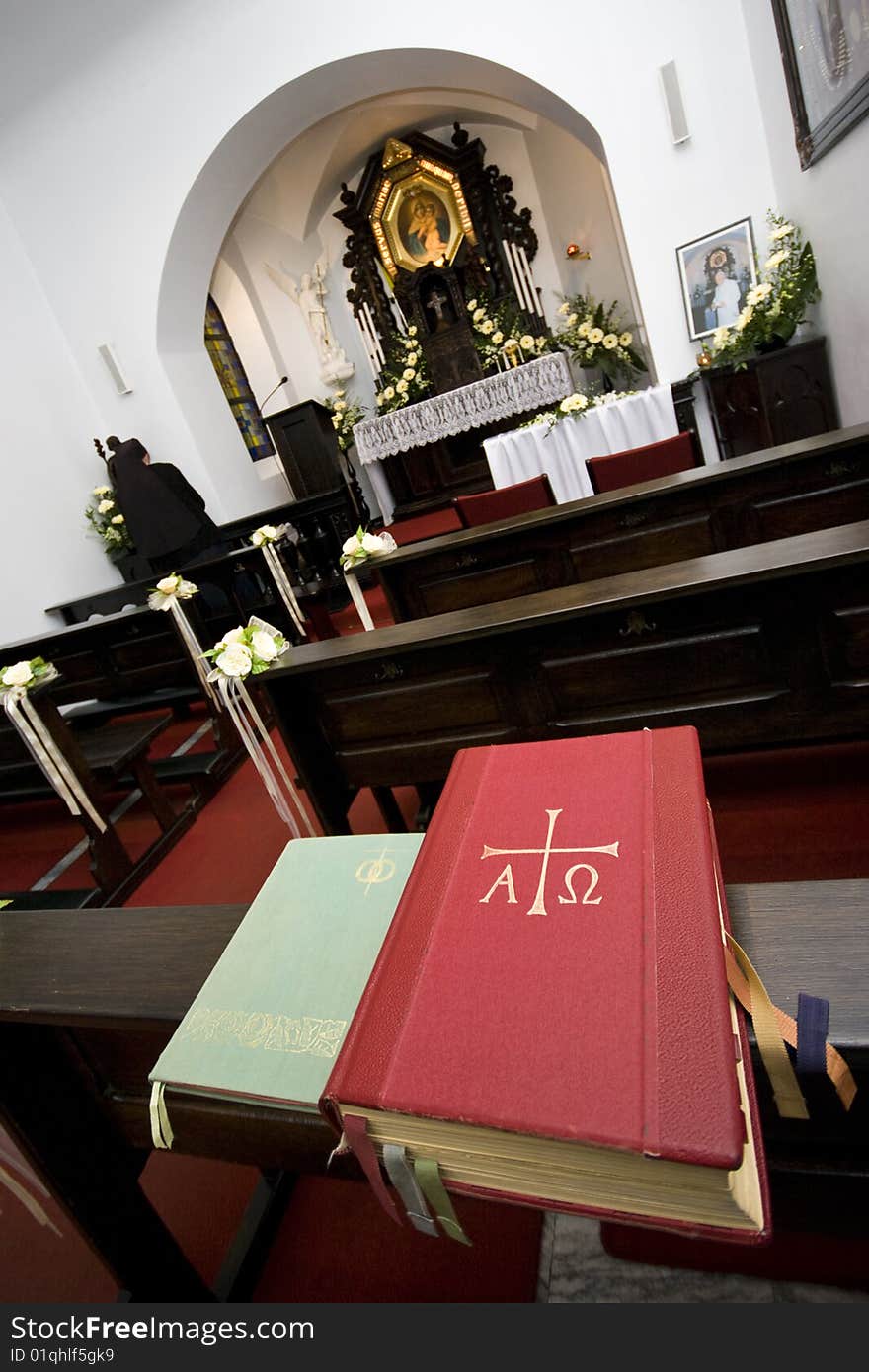 Interior of a small Roman catholic chapel with a nun praying at the side of the altar.