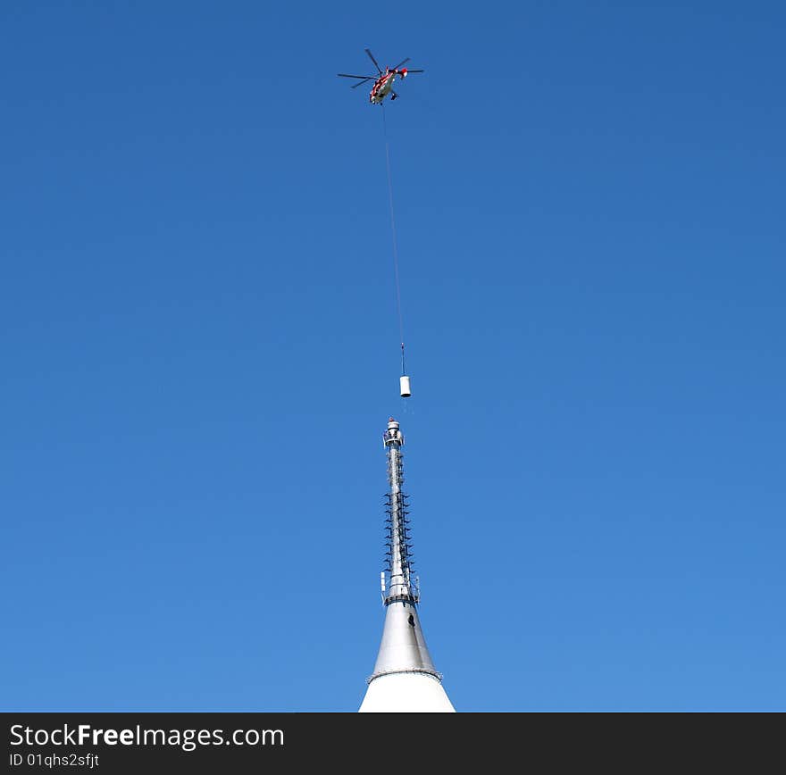 The helicopter settles on top of a television antenna towers new part. The helicopter settles on top of a television antenna towers new part.