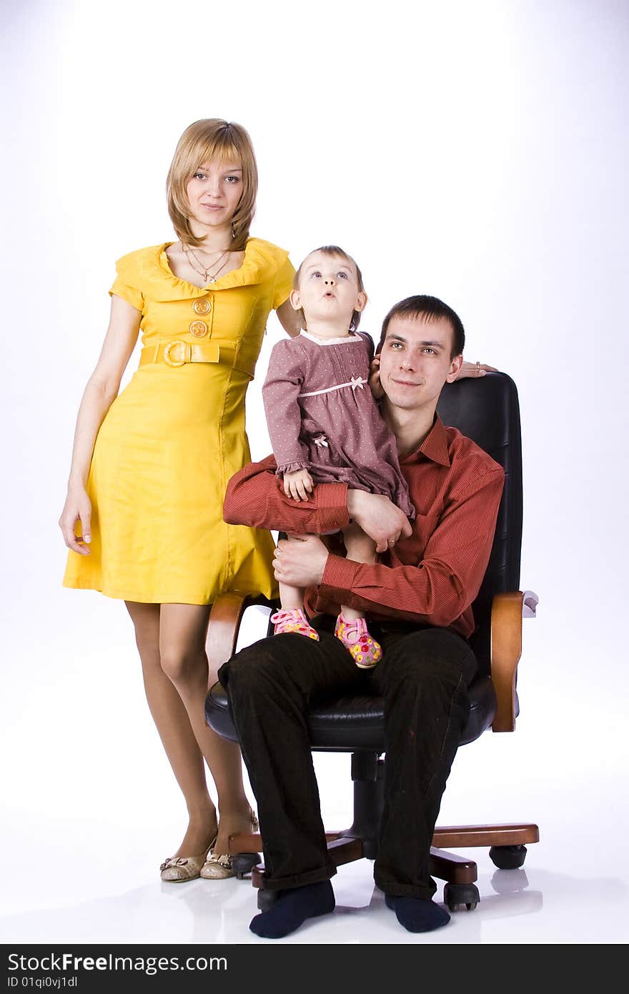 The child sits in an office chair. Mother is beside the child, dad is sitting with a daughter.