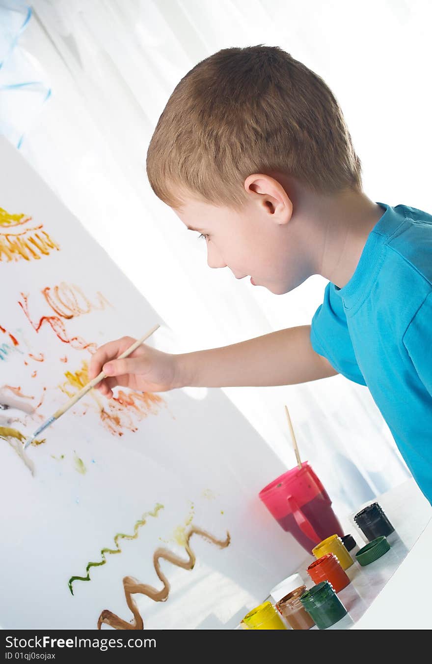 The boy draws with interest paints on a white cloth