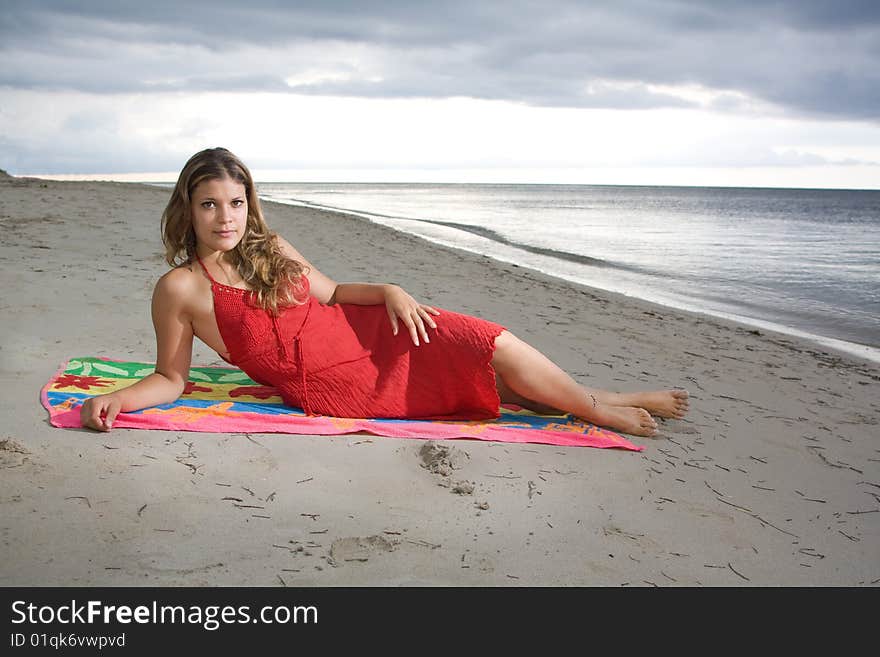 Attractive girl laying on a towel with red dress, at beach sunset