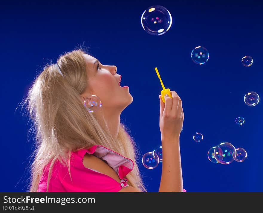 Young beautiful blond inflate soap bubbles on a blue background