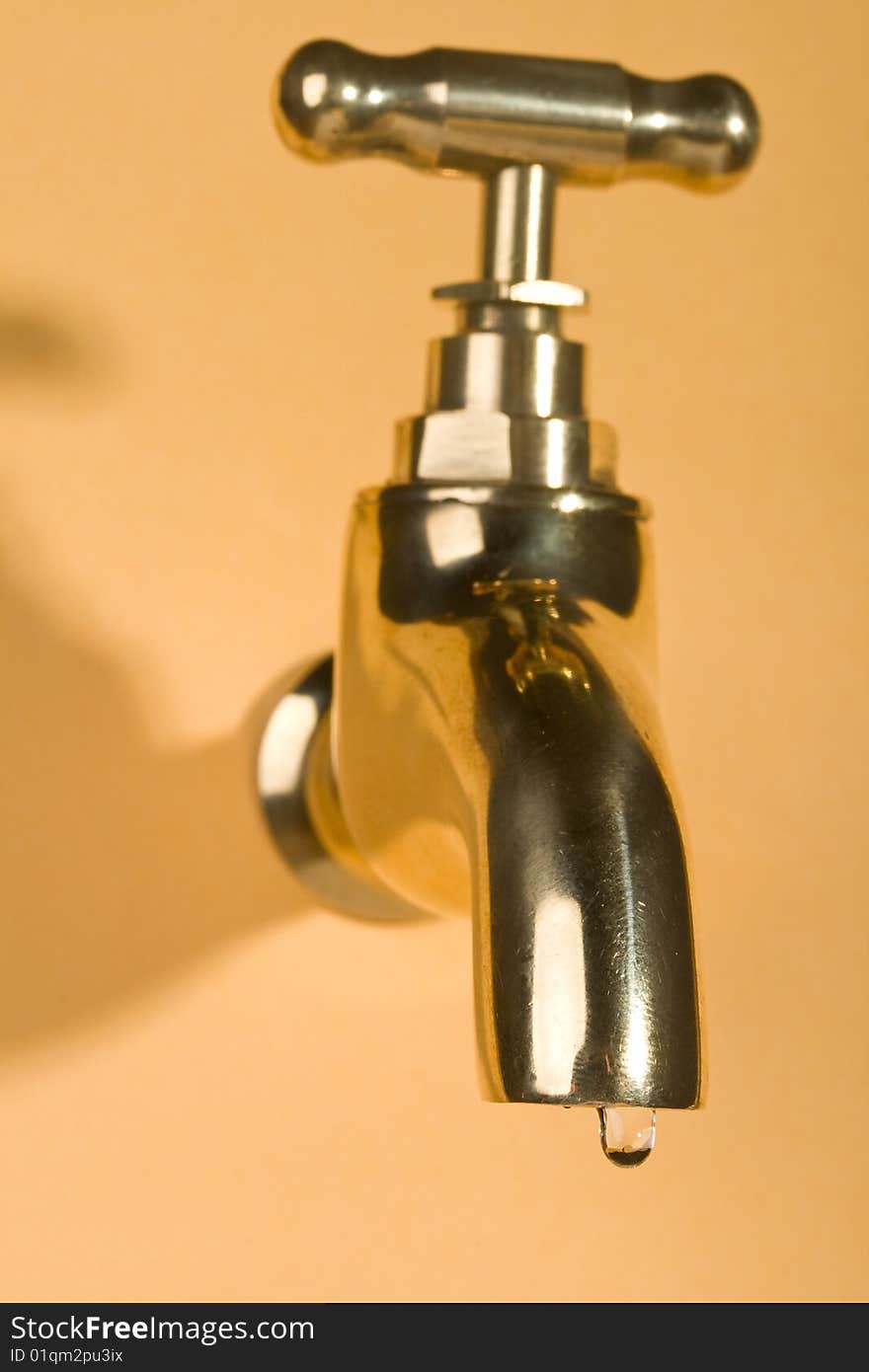 Close-up gold faucet in orange wall with water drop. Close-up gold faucet in orange wall with water drop