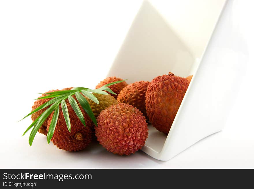 Lychee and green leaf spilling out a dish with clipping on a white background. Lychee and green leaf spilling out a dish with clipping on a white background