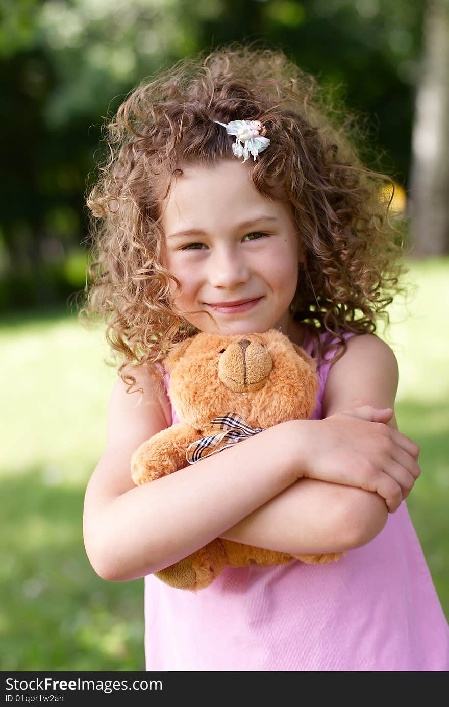 The beautiful girl of 7 years embraces a teddy bear on a green vegetative background in the summer. The beautiful girl of 7 years embraces a teddy bear on a green vegetative background in the summer