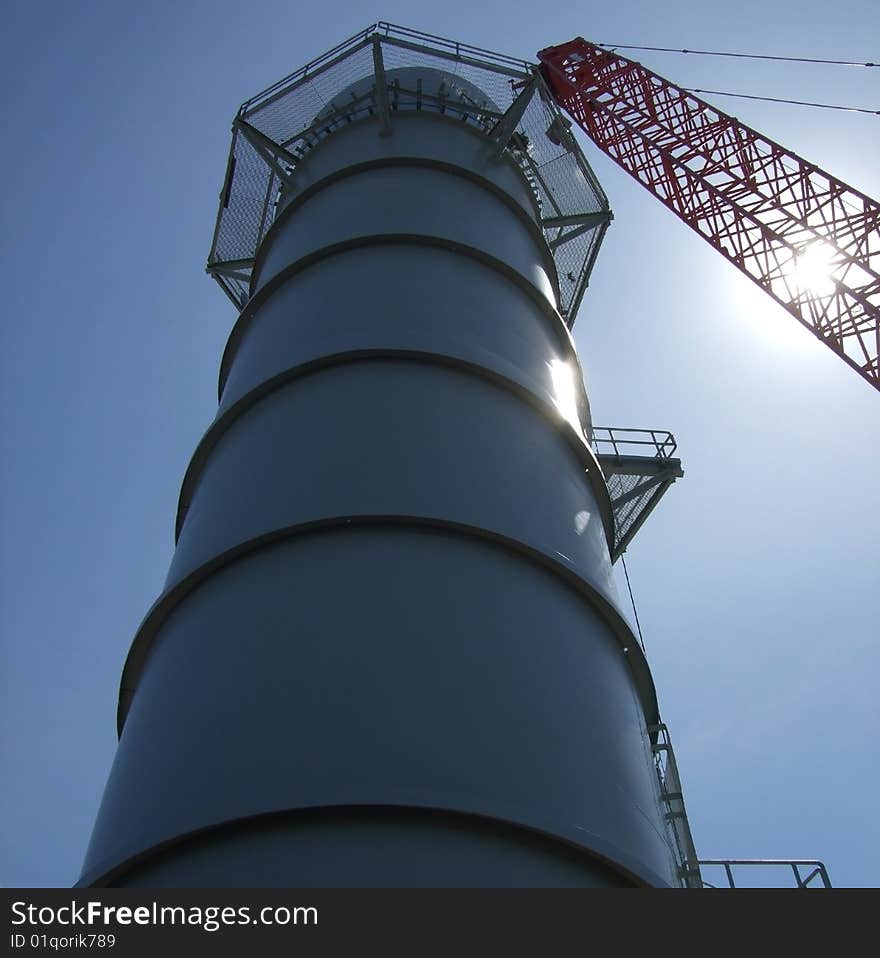 Smoke stack with crane through sun