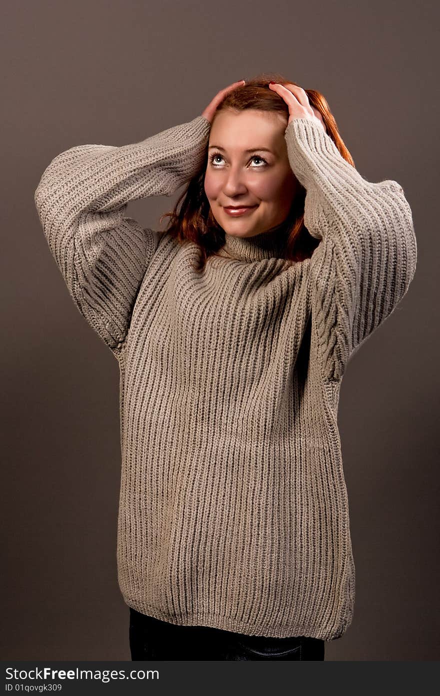 Smiling red haired woman in sweater isolated over gray