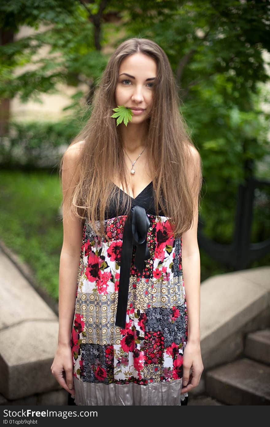 Beautiful girl with a maple leaf in her mouth. Green leaves  background.