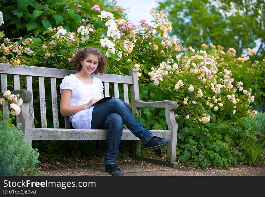 The girl with the open book sits on a bench and smiles. The girl with the open book sits on a bench and smiles