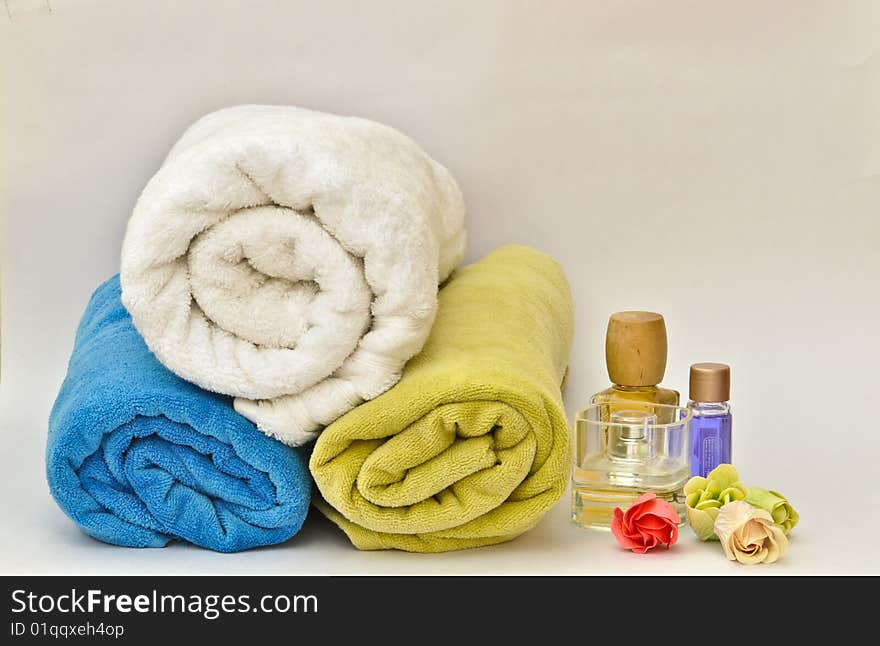 Colorful towels stacked on each other beside bottles of perfumes and lotions and among flowers. Colorful towels stacked on each other beside bottles of perfumes and lotions and among flowers