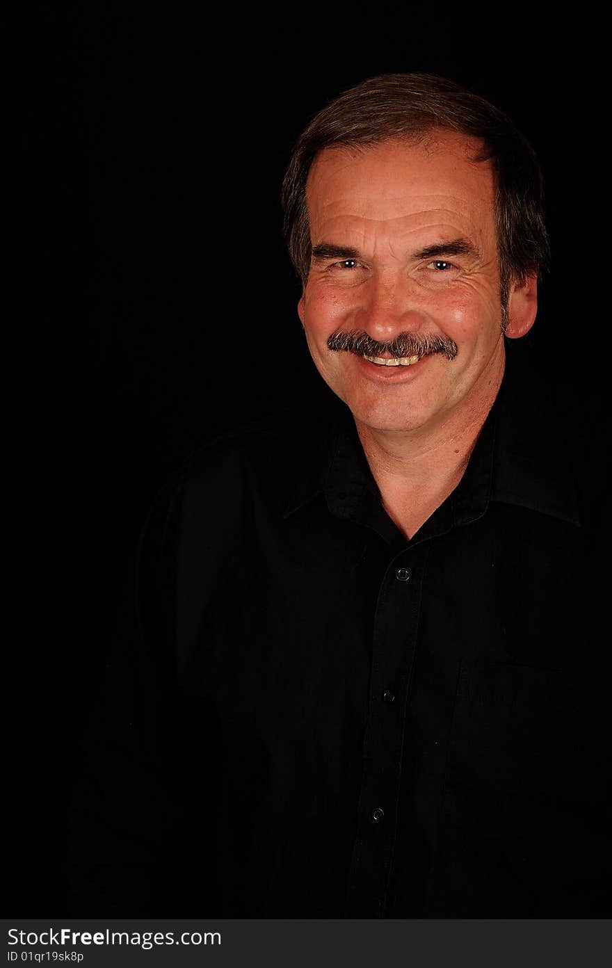 A smiling man on a black studio back ground