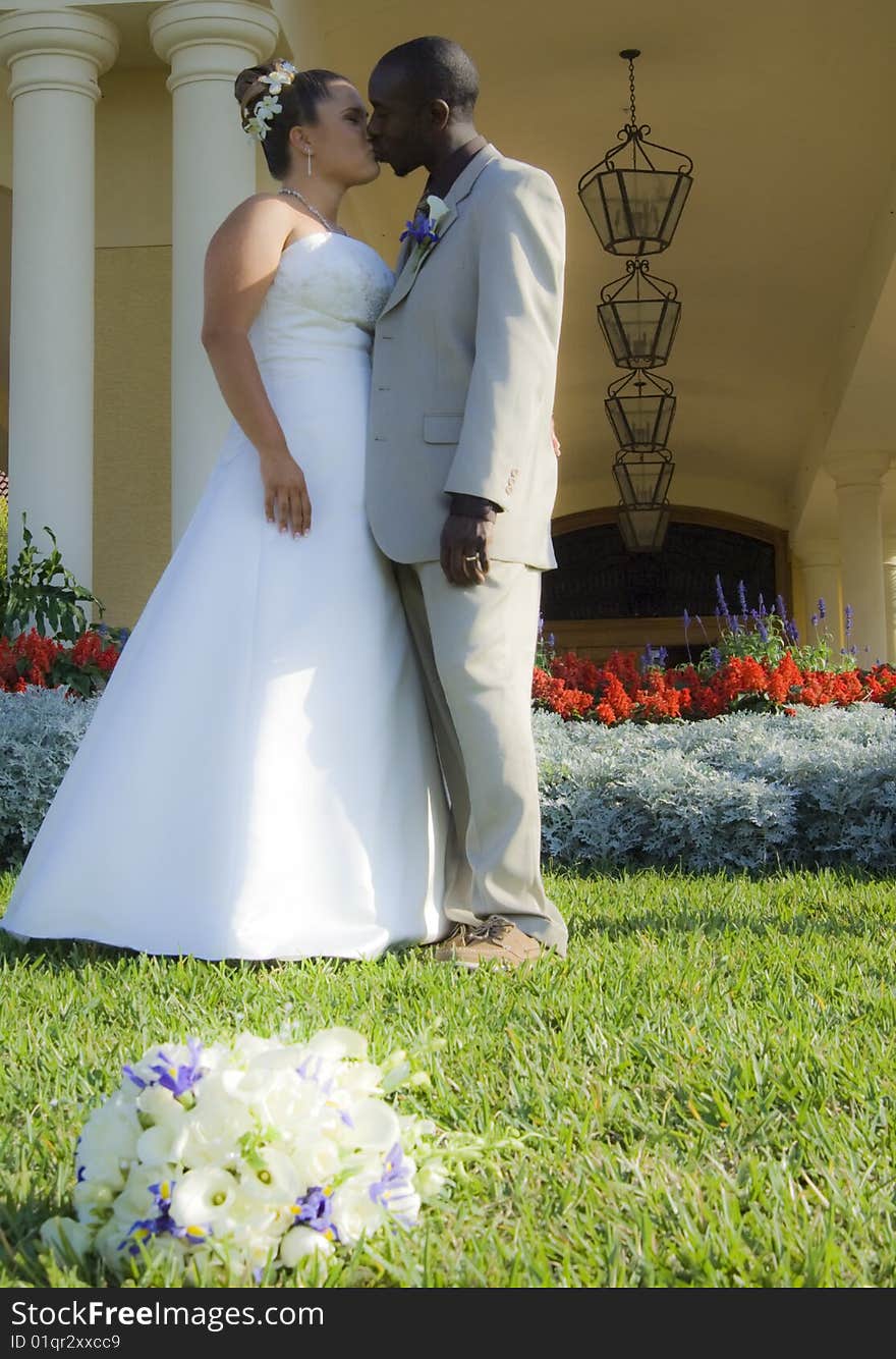 A bride and groom kissing in front of country club with bouquet of flowers in grass. A bride and groom kissing in front of country club with bouquet of flowers in grass.