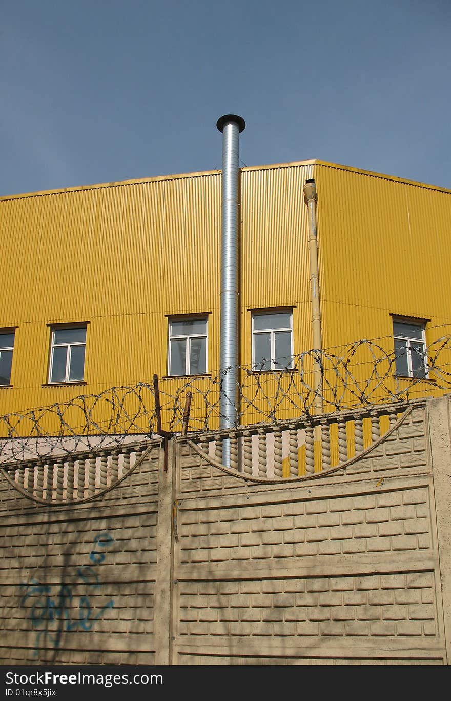 A secured industrial zone with concrete fence and barbed wire on the blue sky background.