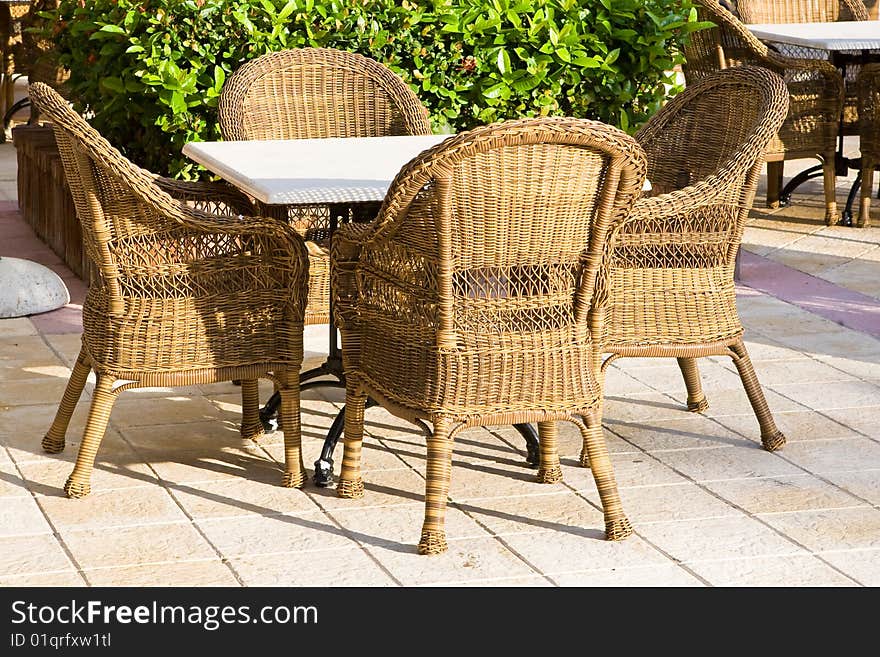 Table and four chairs on patio near bush and grass