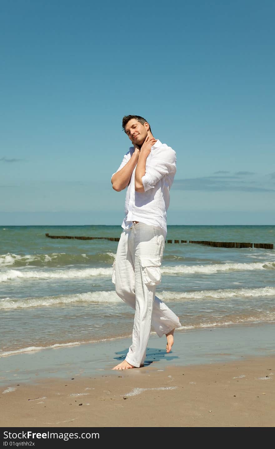 Man walking down the coast feeling carefree and free . relaxing with hands on head . little waves in background. Man walking down the coast feeling carefree and free . relaxing with hands on head . little waves in background