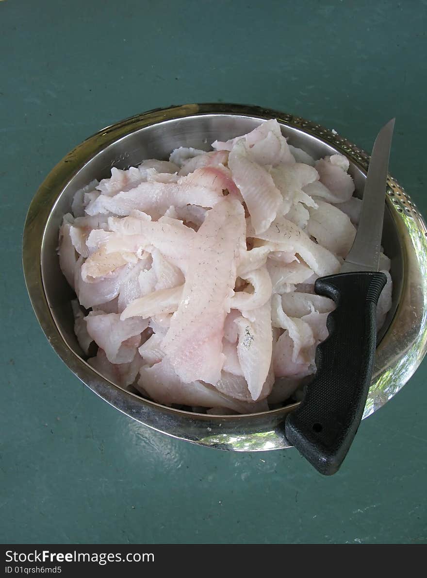 A stainless steel bowl filled with crappie fillets & fillet knife