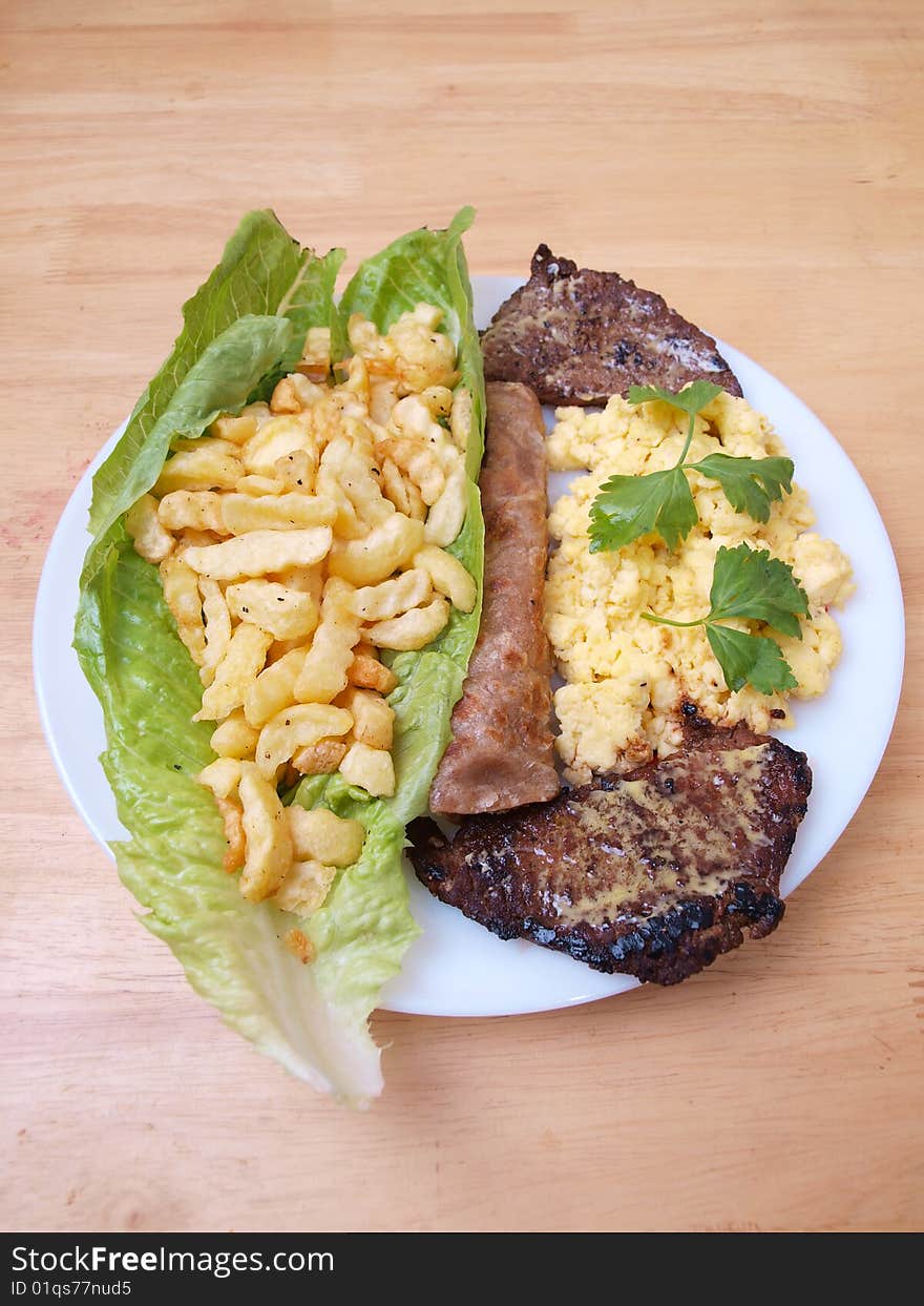 Plate of roasted beef cutlets salad fries eggs and bread on wood table surface. Plate of roasted beef cutlets salad fries eggs and bread on wood table surface