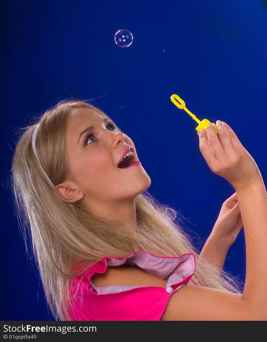 Young beautiful blond inflate soap bubbles on a blue background