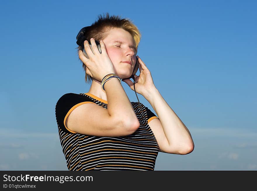 Young girl listining music on a blue sky background. Young girl listining music on a blue sky background