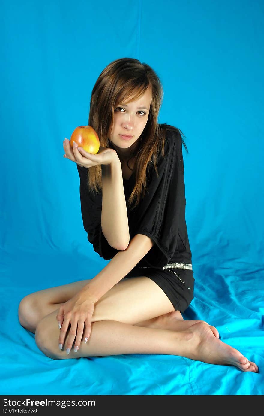 Girl holds in the hand apple survey in the studio against the blue
background. Girl holds in the hand apple survey in the studio against the blue
background