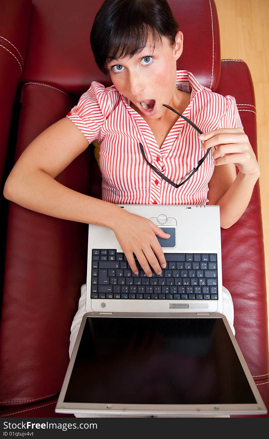 Surprised brunette woman laying on sofa with notebook and glasses with hands on keyboard and wide open mouth looking into the camera. Surprised brunette woman laying on sofa with notebook and glasses with hands on keyboard and wide open mouth looking into the camera