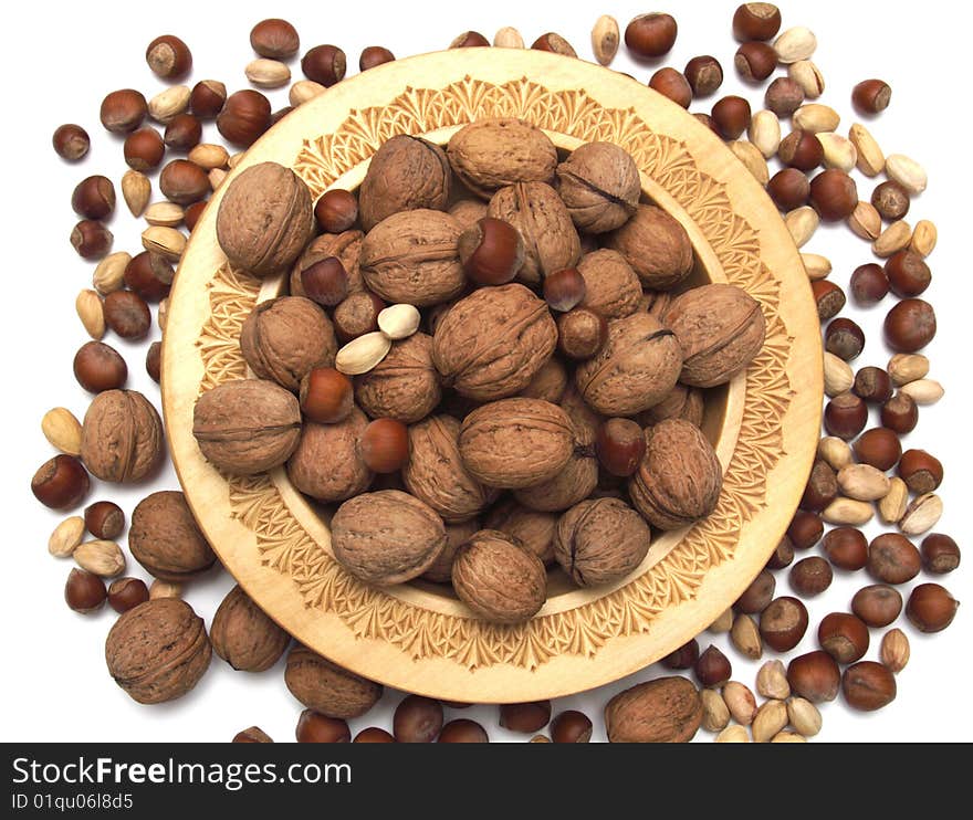 Walnuts, pistachioes, hazelnuts in a wooden plate on a white background.