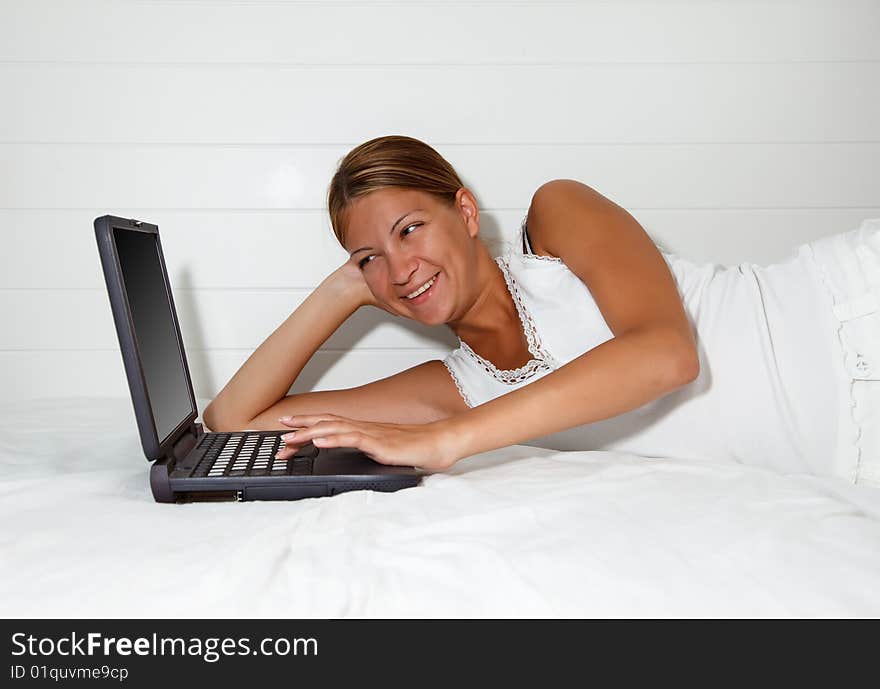 Pretty young woman laying down on bed and working at computer. Pretty young woman laying down on bed and working at computer