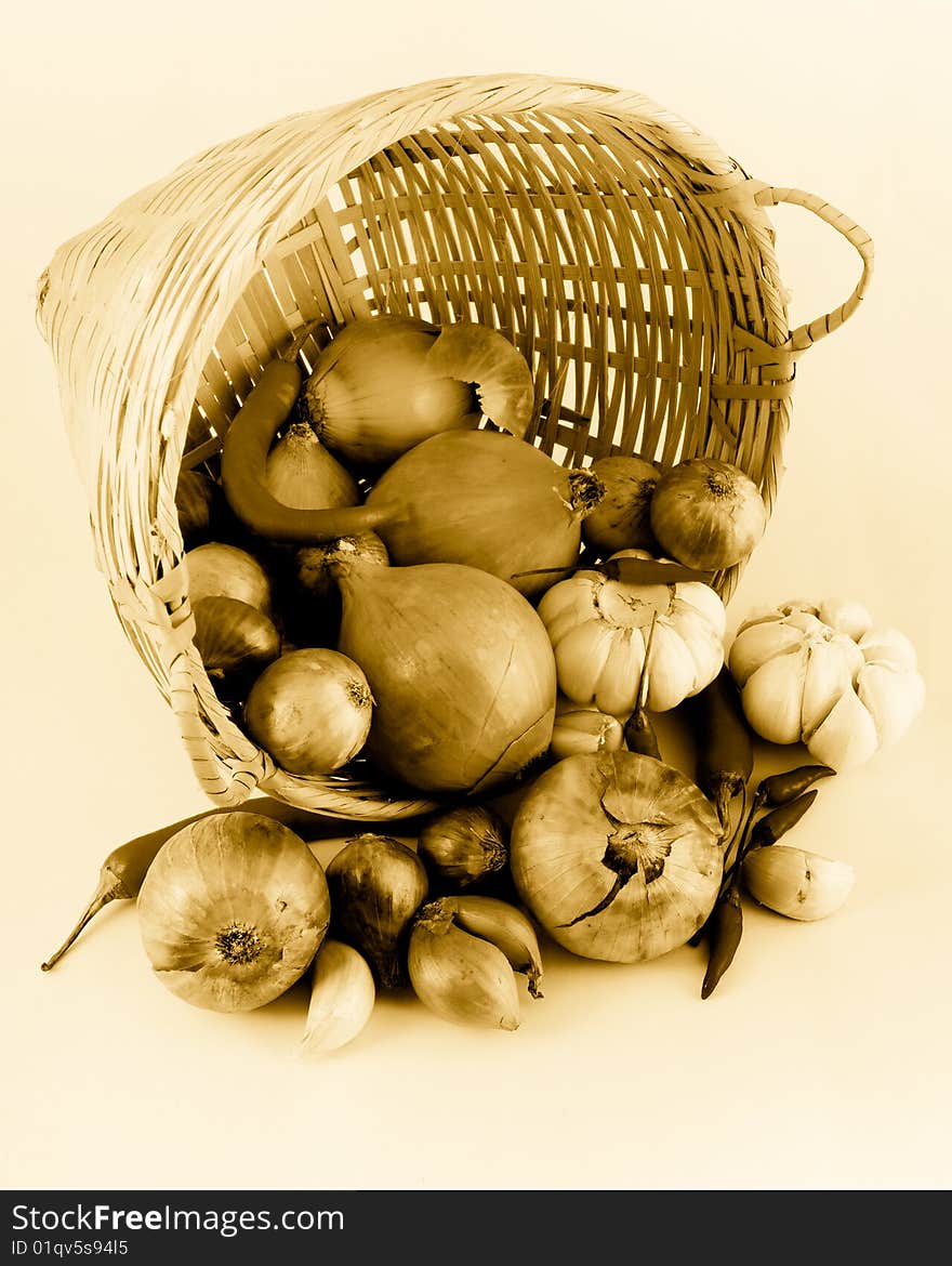 Still life of a onions, garlic and chilies tumbling from a rattan basket, in golden tones