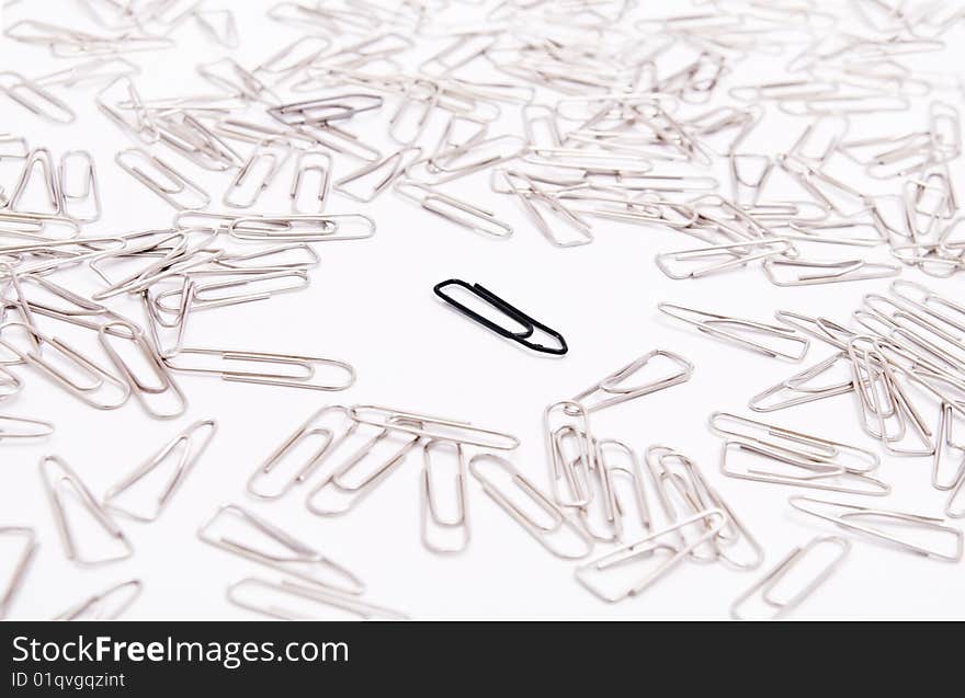 One black paperclip among many steel grey paperclips on white background. One black paperclip among many steel grey paperclips on white background