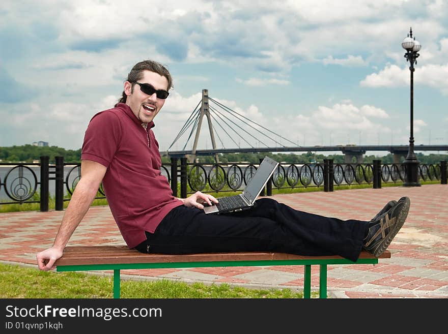 Young man sitting on a park bench with his laptop. Young man sitting on a park bench with his laptop