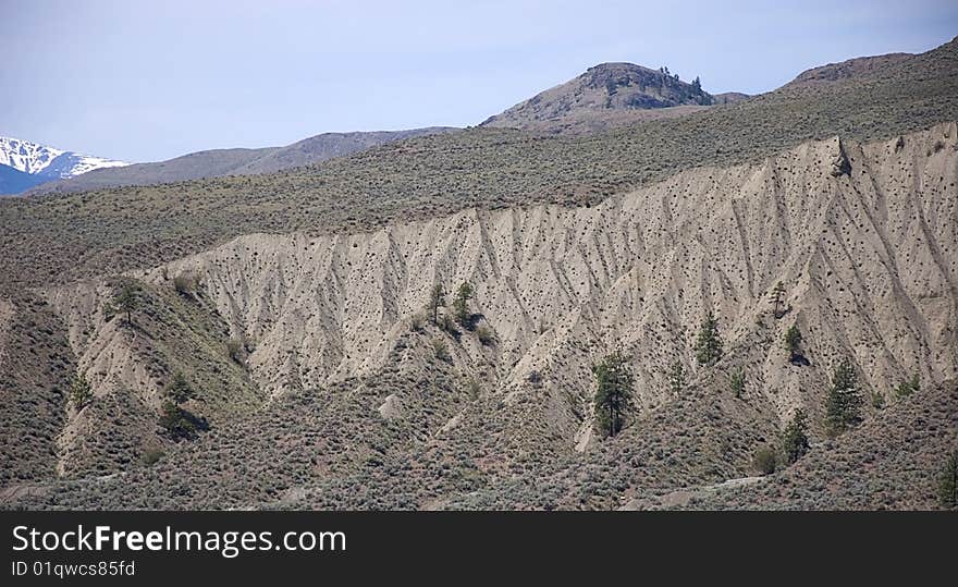 This arid desert rugged landscape is beautiful with snow capped mountains and blue sky in the background show lots of interesting patterns and lines in the setting of sparse trees and sagebrush. This arid desert rugged landscape is beautiful with snow capped mountains and blue sky in the background show lots of interesting patterns and lines in the setting of sparse trees and sagebrush.