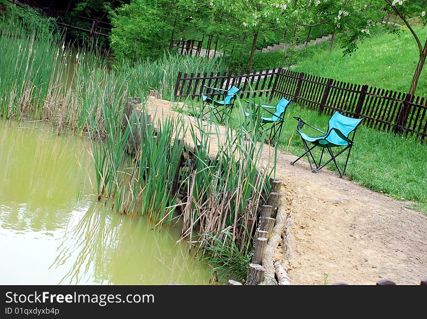 Folding blue chairs by muddy yellowish pond. Folding blue chairs by muddy yellowish pond