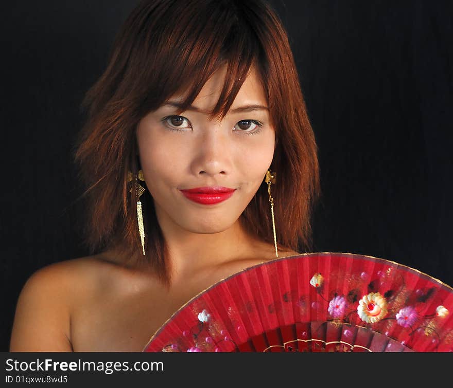 Very seductive young asian woman with a fan on a black background