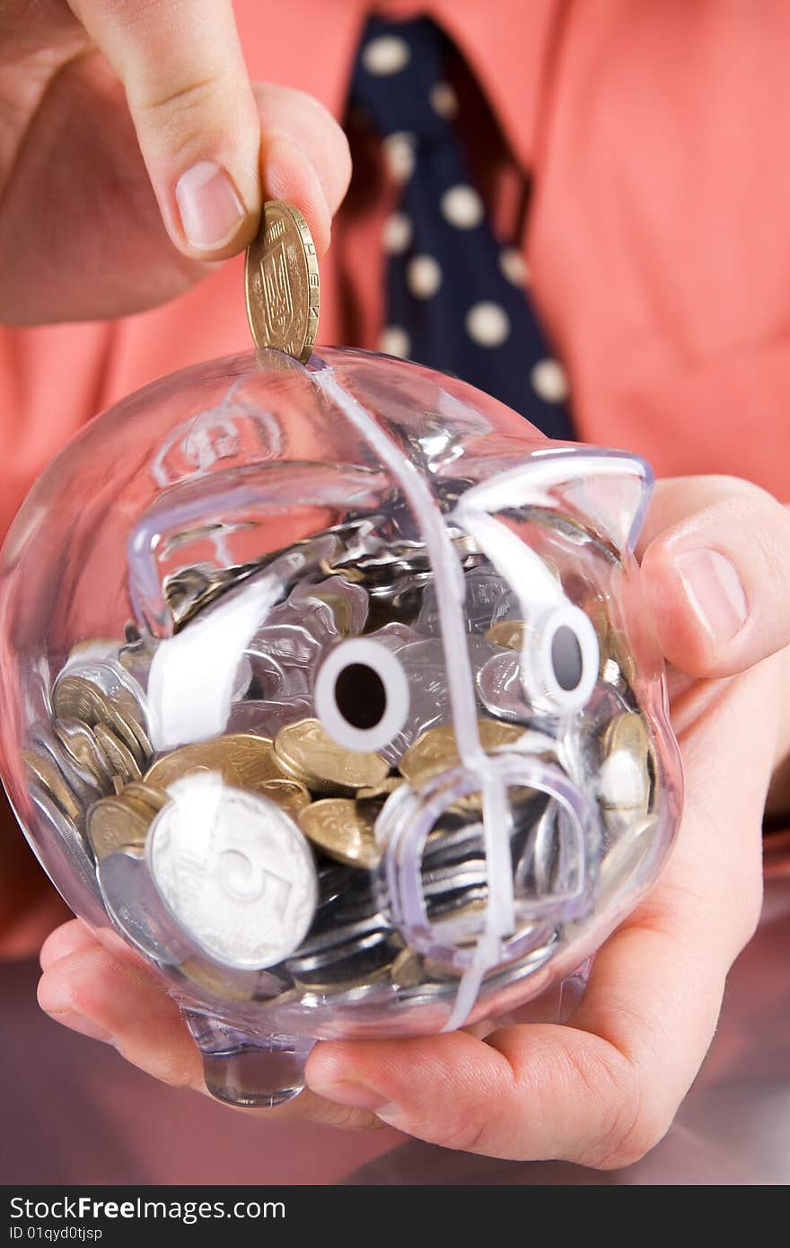 Businessman inserting coin into transparent piggy bank