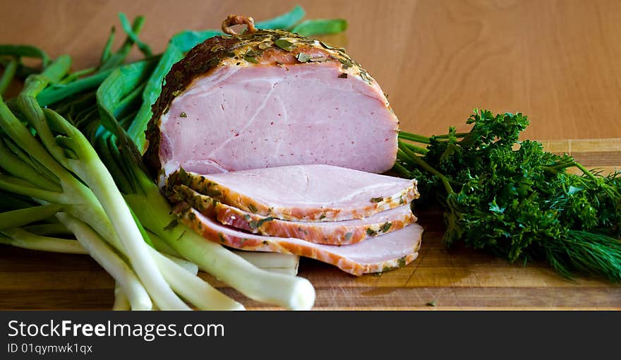 Appetizing slices of ham with potherbs on the kitchen table. Appetizing slices of ham with potherbs on the kitchen table