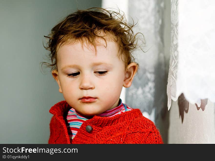 A  broody little boy  with dishevelled blond  hair on the light background